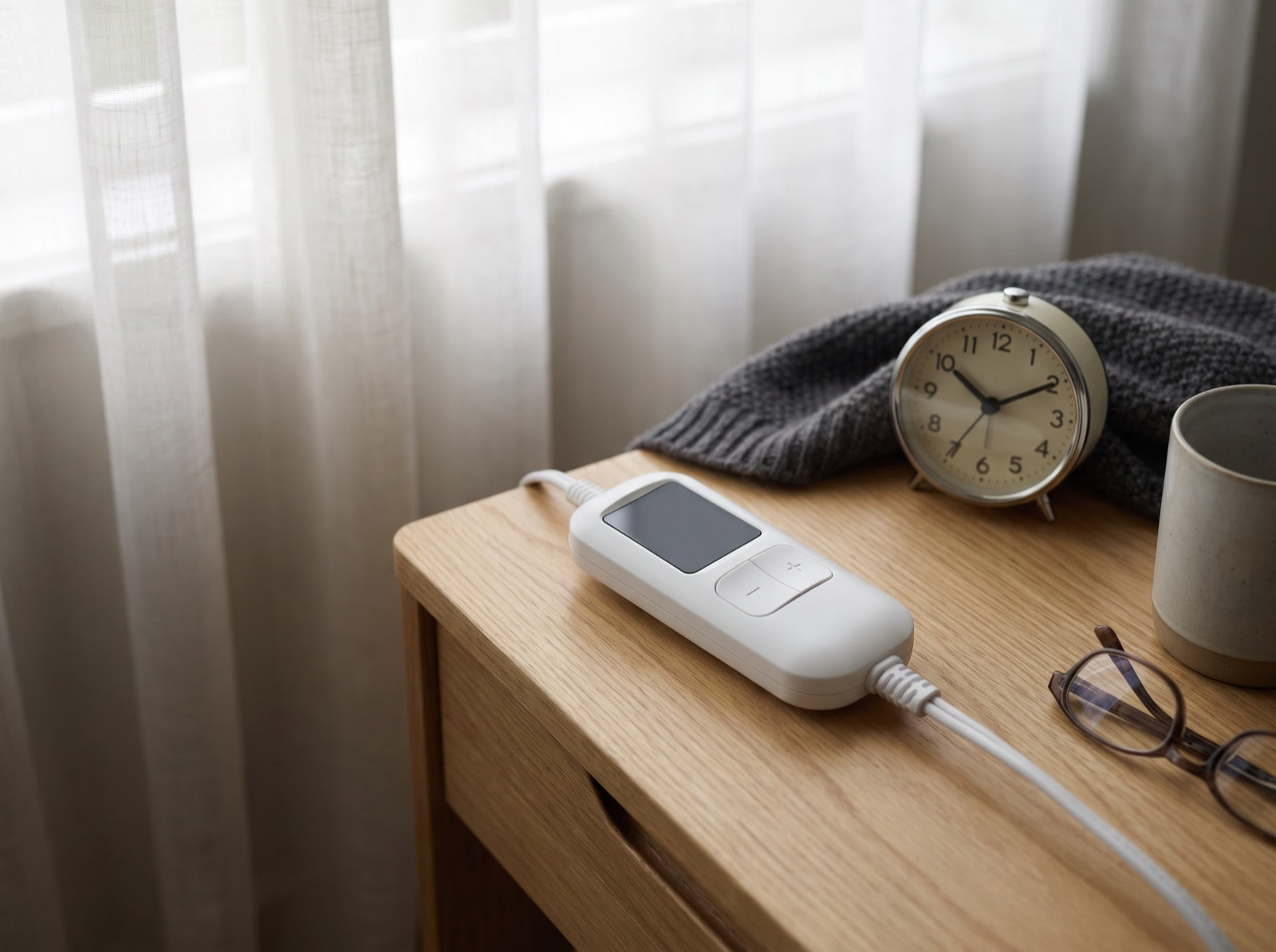 A heated throw controller on a bedside table next to an alarm clock