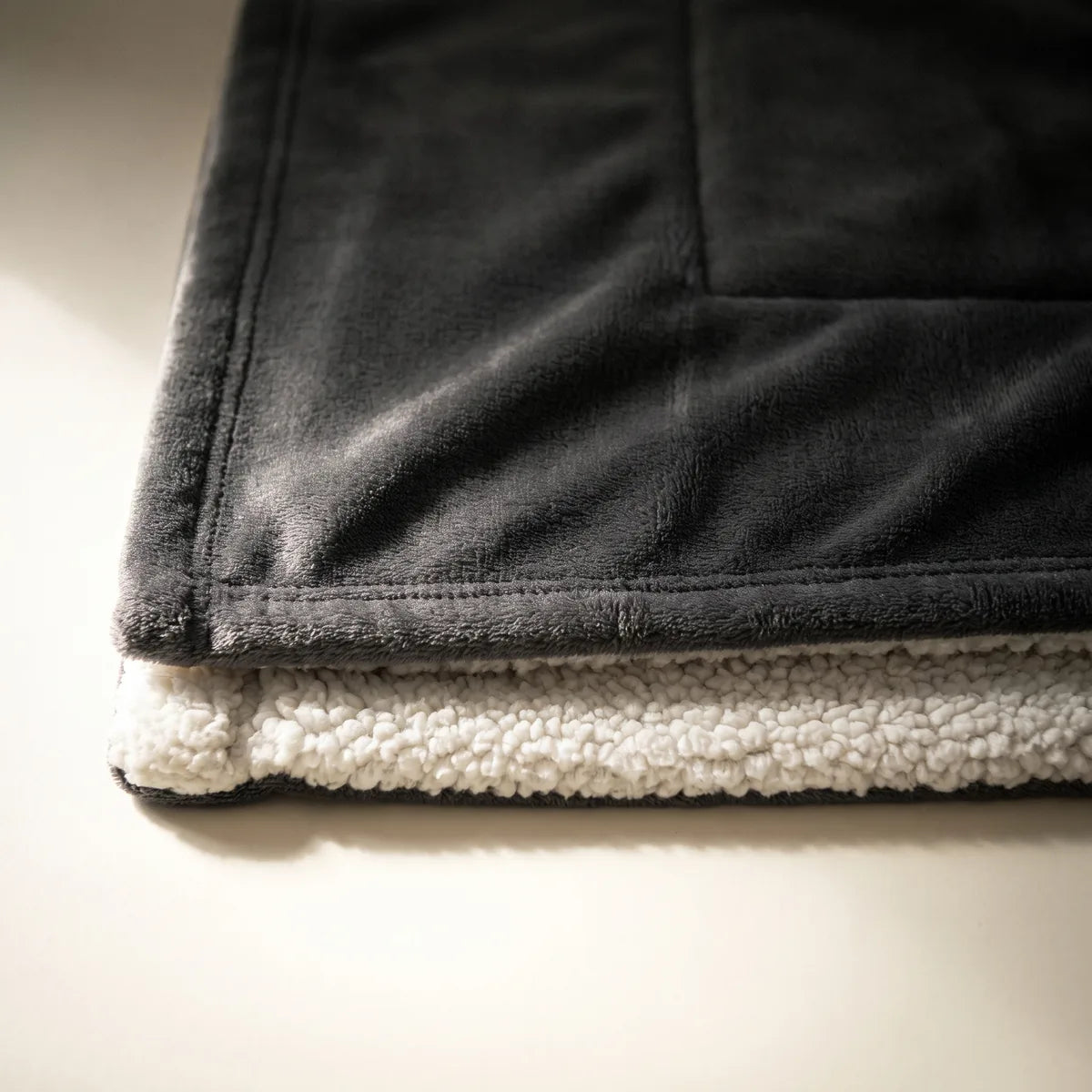 Close view of the Signature Heated Throw in Anthracite: the anthracite fleece face above the cream sherpa reverse.